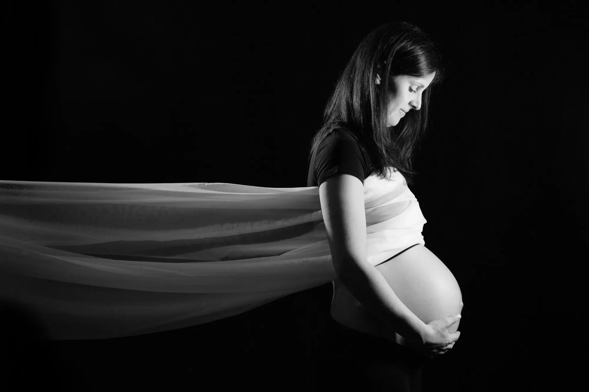 Die Silhouette einer werdenden Mutter mit einem halbdurchsichtigen Tuch zum linken Bildrand gespannt.