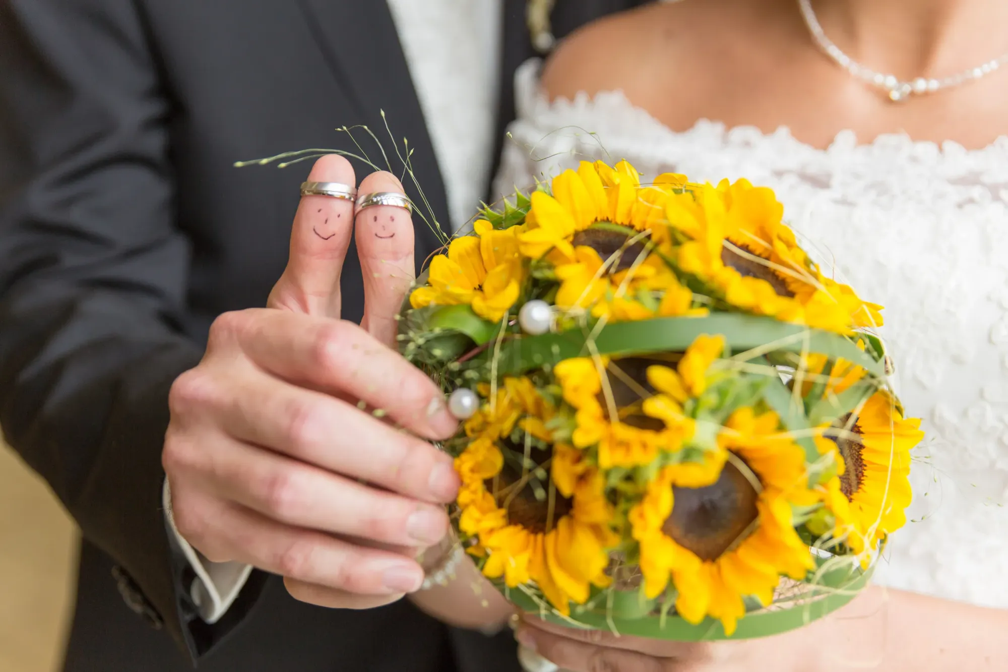 Ein Brautpaar mit Ringen und aufgezeichnetem Gesicht auf den Daumen.