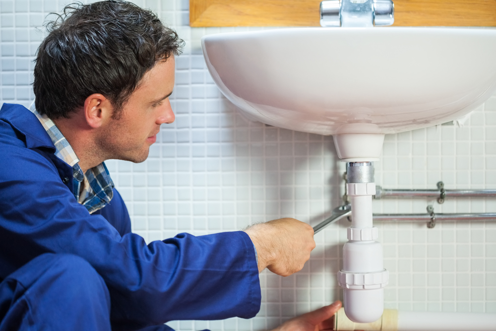 Handsome happy plumber repairing sink in public bathroom