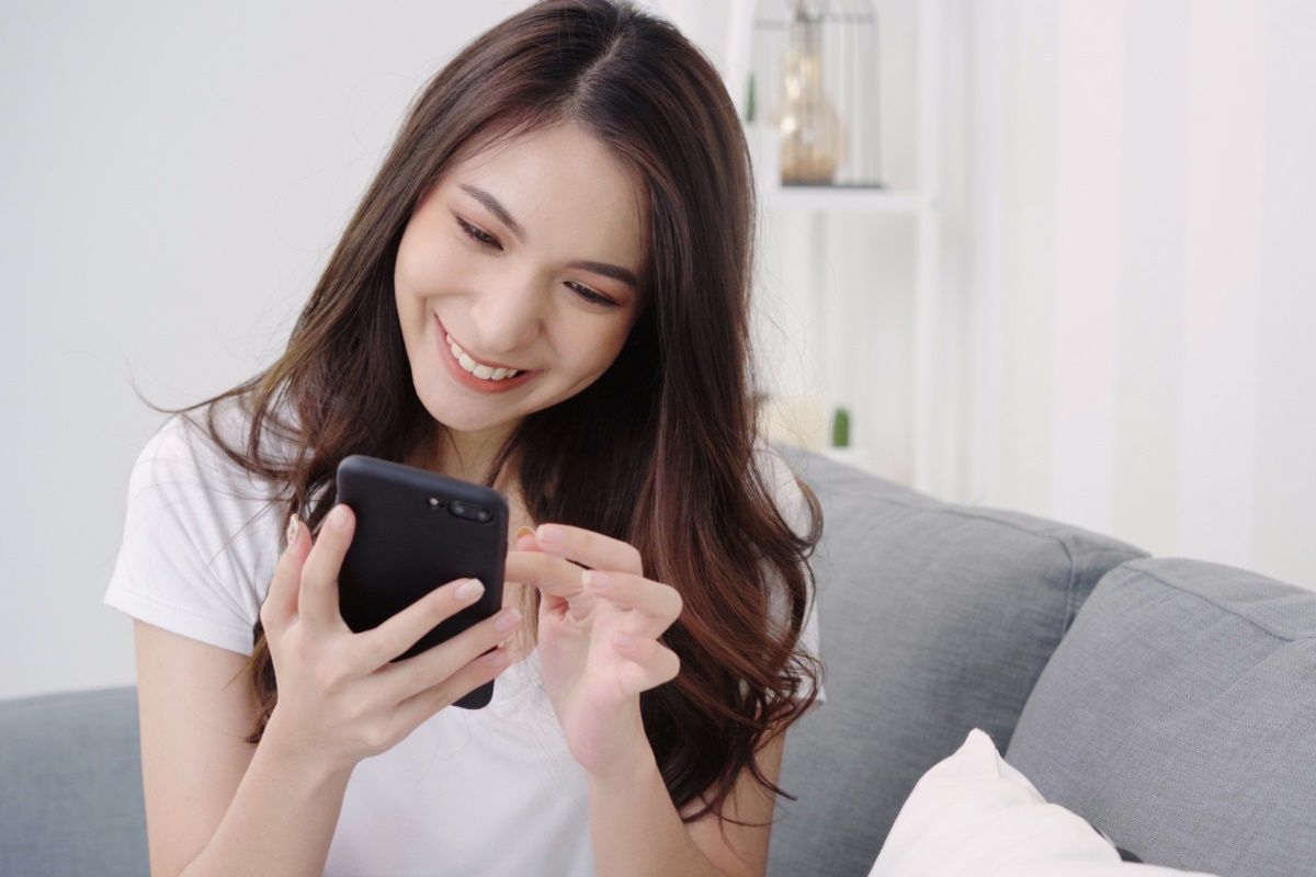 asian-woman-playing-smartphone-while-lying-home-sofa-her-living-room