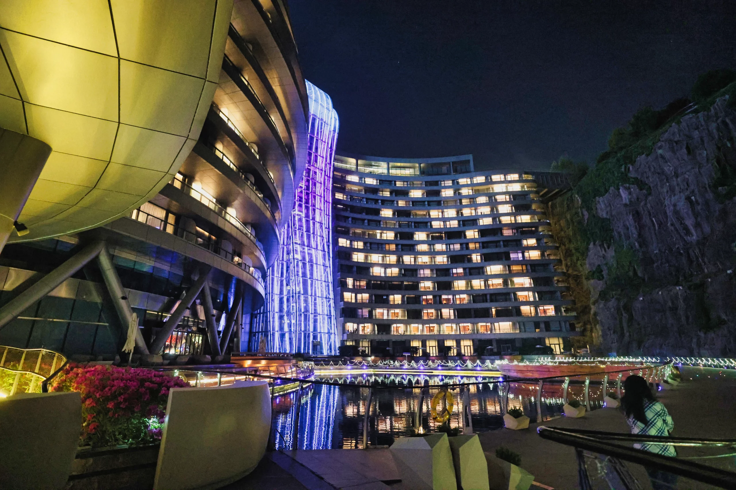 Hotel illuminated at night with light reflections on water.