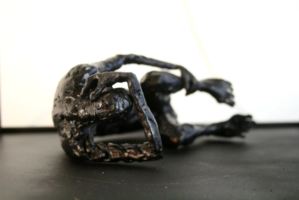 A curled metal figure on its side, with thick irregular surfaces and a rectangular frame.