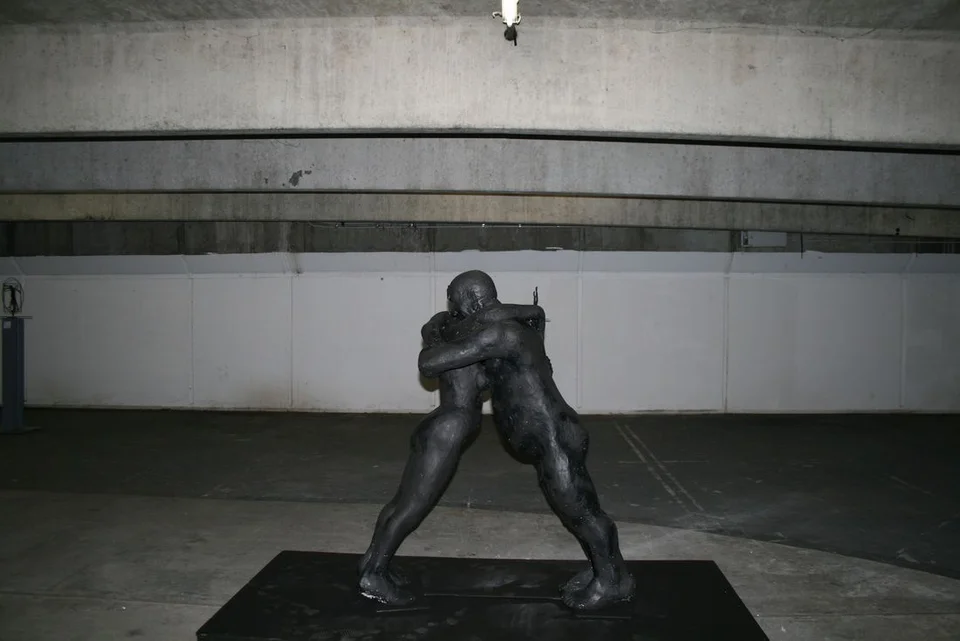 Two large intertwined figures on a low platform in a spacious interior.