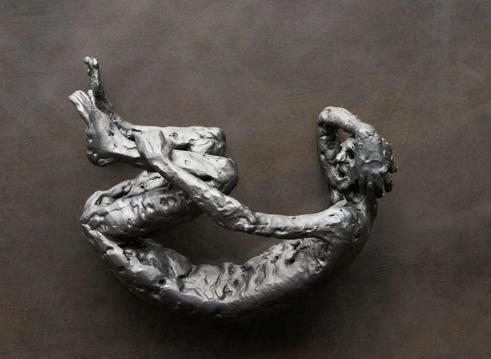A curled metal figure on its side, with thick irregular surfaces and a rectangular frame.