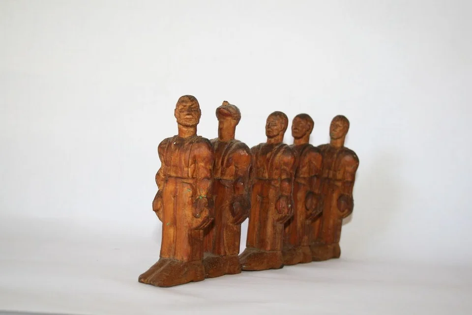 A row of small upright carved wooden figures on a shared rectangular base.