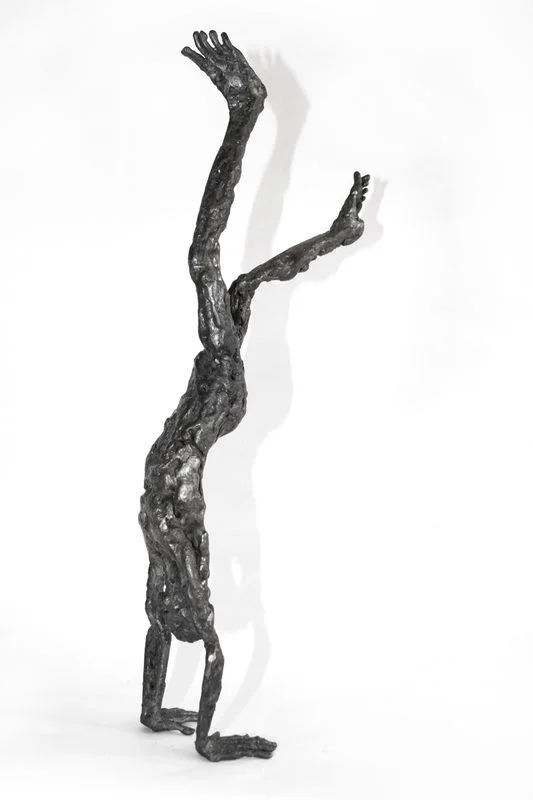 A rough-surfaced steel figure balancing upside down on its hands.