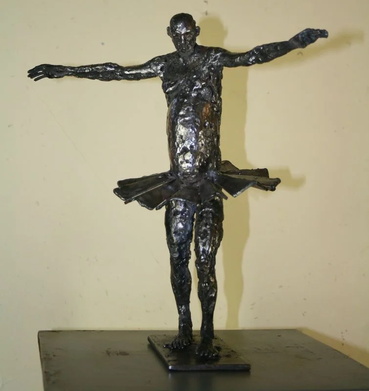 A steel figure with arms outstretched and angular pieces around its waist.