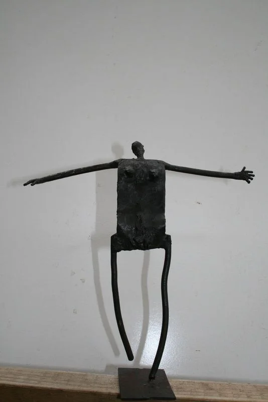 A steel figure with a rectangular torso, long narrow legs and raised or extended arms.