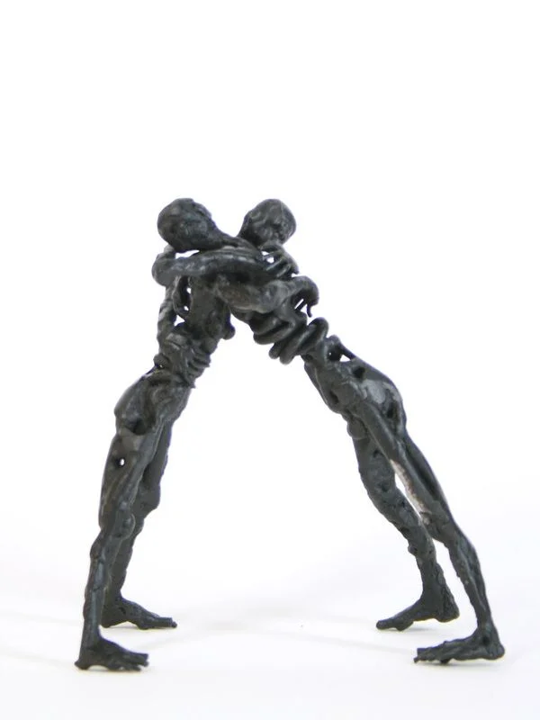 Two steel figures leaning into one another, arms joined and legs braced apart.
