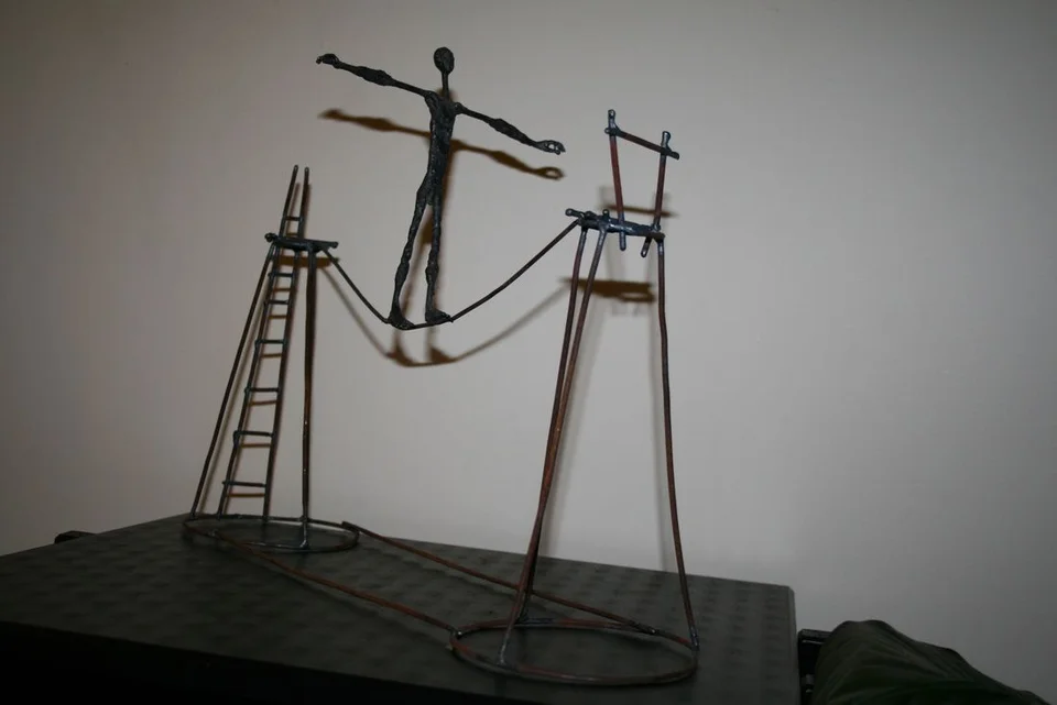 A small wire figure on a suspended rope between two tall supports and ladders.