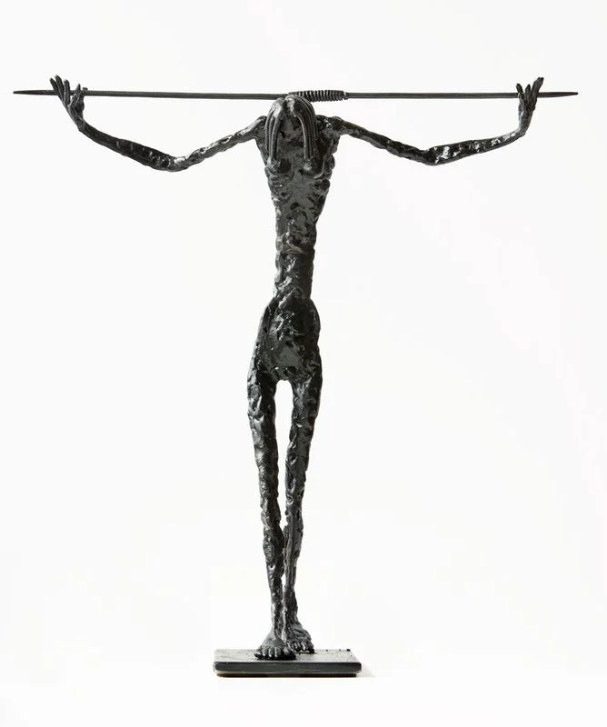 A tall steel figure holding a long rod across its shoulders.