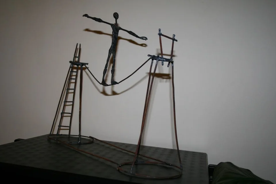 A small wire figure on a suspended rope between two tall supports and ladders.