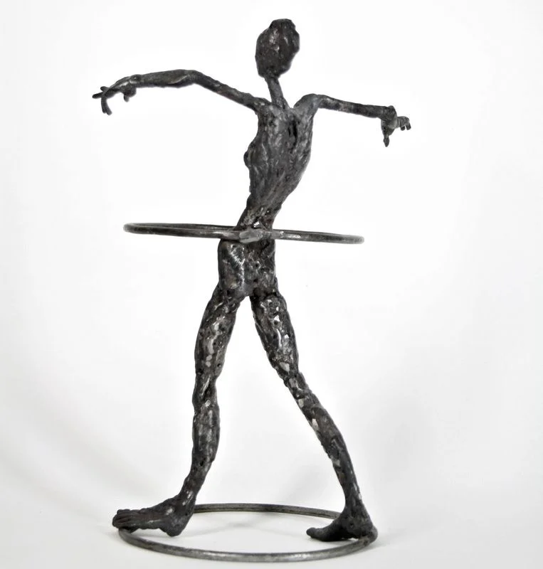 A slender steel figure with arms extended and a hoop around its waist.