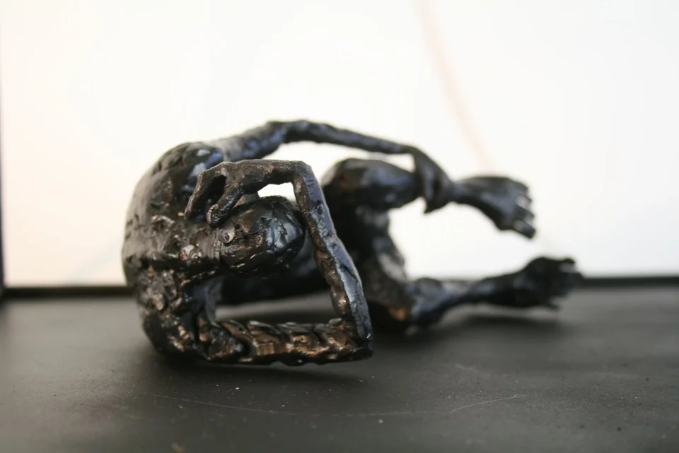 A curled metal figure on its side, with thick irregular surfaces and a rectangular frame.