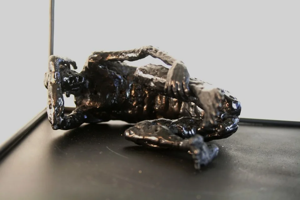 A curled metal figure on its side, with thick irregular surfaces and a rectangular frame.