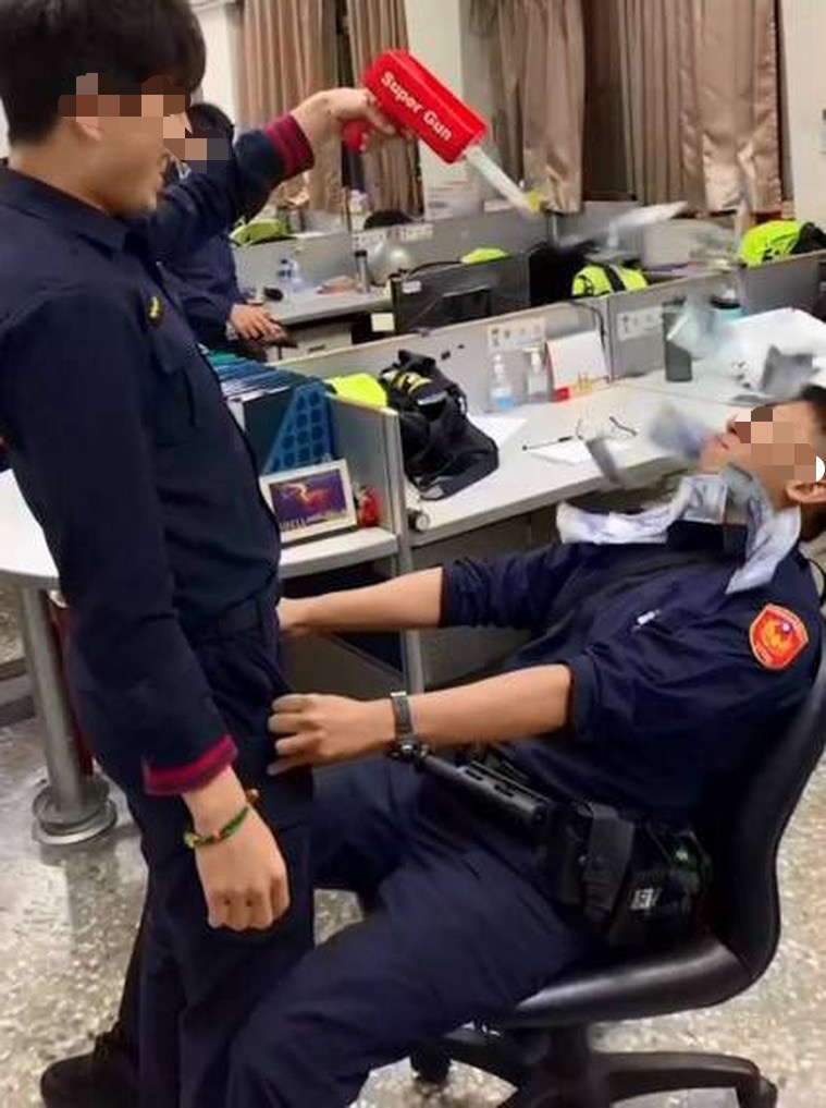 有一名員警拿著玩具鈔票槍，對著坐在椅子上的另名員警噴射。（圖／翻攝自「社會事新聞群」）