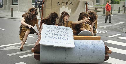 Six cavemen in a Flintstones-style car protesting about the car industry's lack of action on climate change