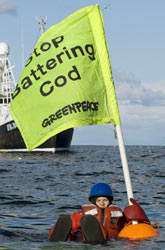 A Greenpeace activist floats in the North Sea with a banner saying 'Stop Battering Cod'