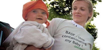 A mother carrying a baby wears a shirt reading "stop contamining my baby!"