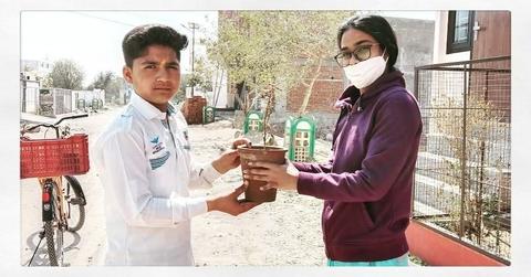A volunteer hands a potted sapling to a young resident