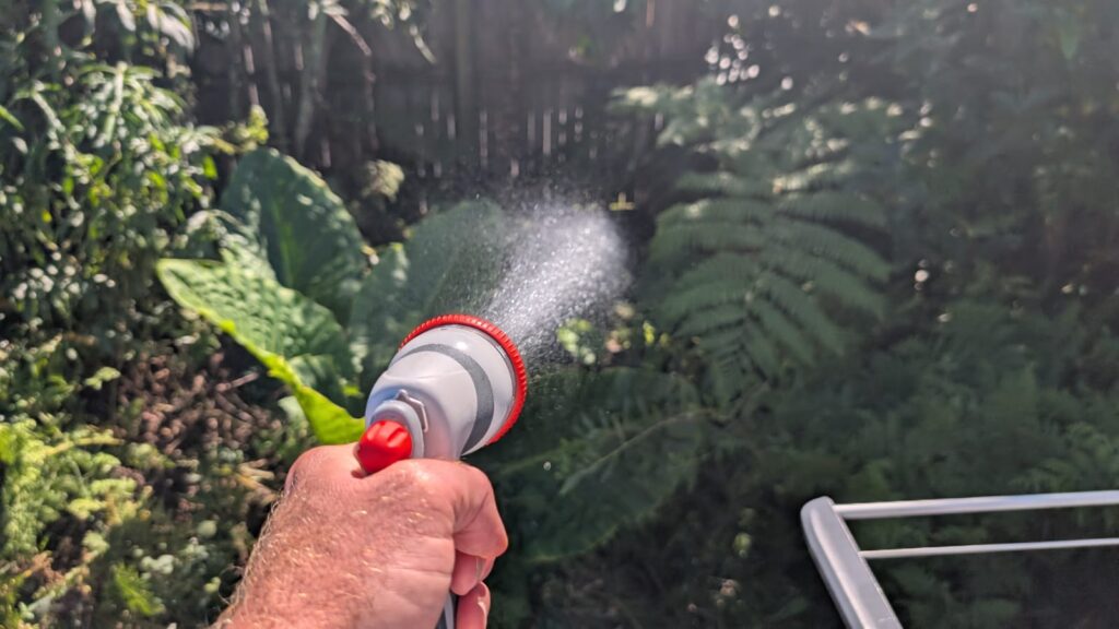 Hand watering garden with hose spray.