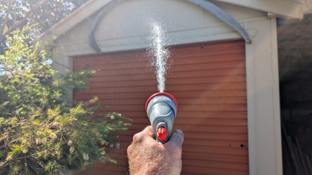 Hand watering plants outside house with hose
