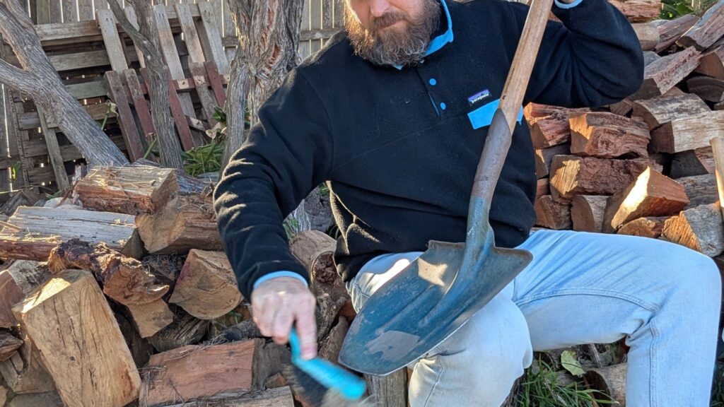 Man cleaning shovel near firewood stack