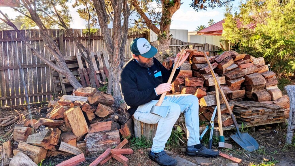 Man inspecting axe by woodpile outdoors