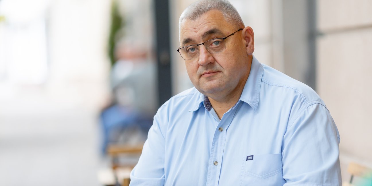 Пан Андрій сидить за столиком в кафе на вулиці, в руках тримає планшет