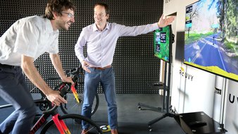 man riding a bicycle indoors in front of a screen with a video projection