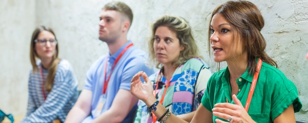 Immagine di un gruppo di persone sedute in un'aula mentre ascoltano una donna che partecipa attivamente alla discussione