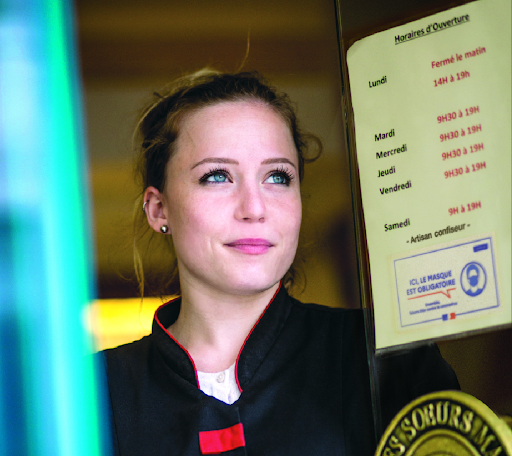 Une commerçante ouvre son magasin. Les horaires sont affichés à l'entrée de son commerce.