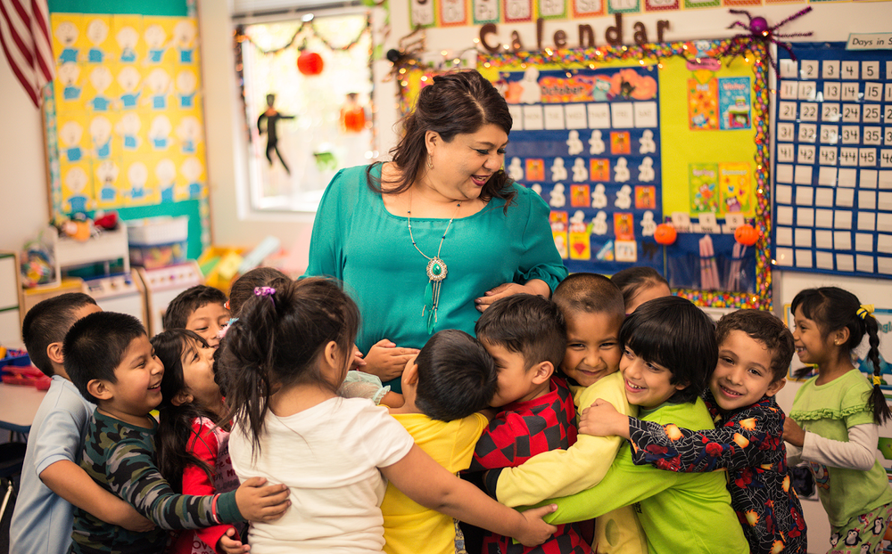 A crowd of primary school children gather in a group hug with their teacher.