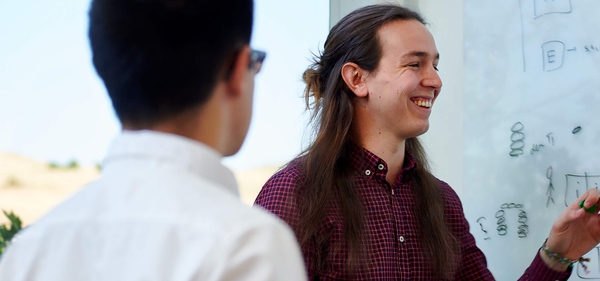 Smiling man presenting ideas on a whiteboard while a colleague attentively observes