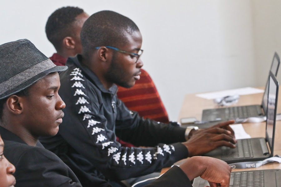 Three men in a row work on online courses on their laptops