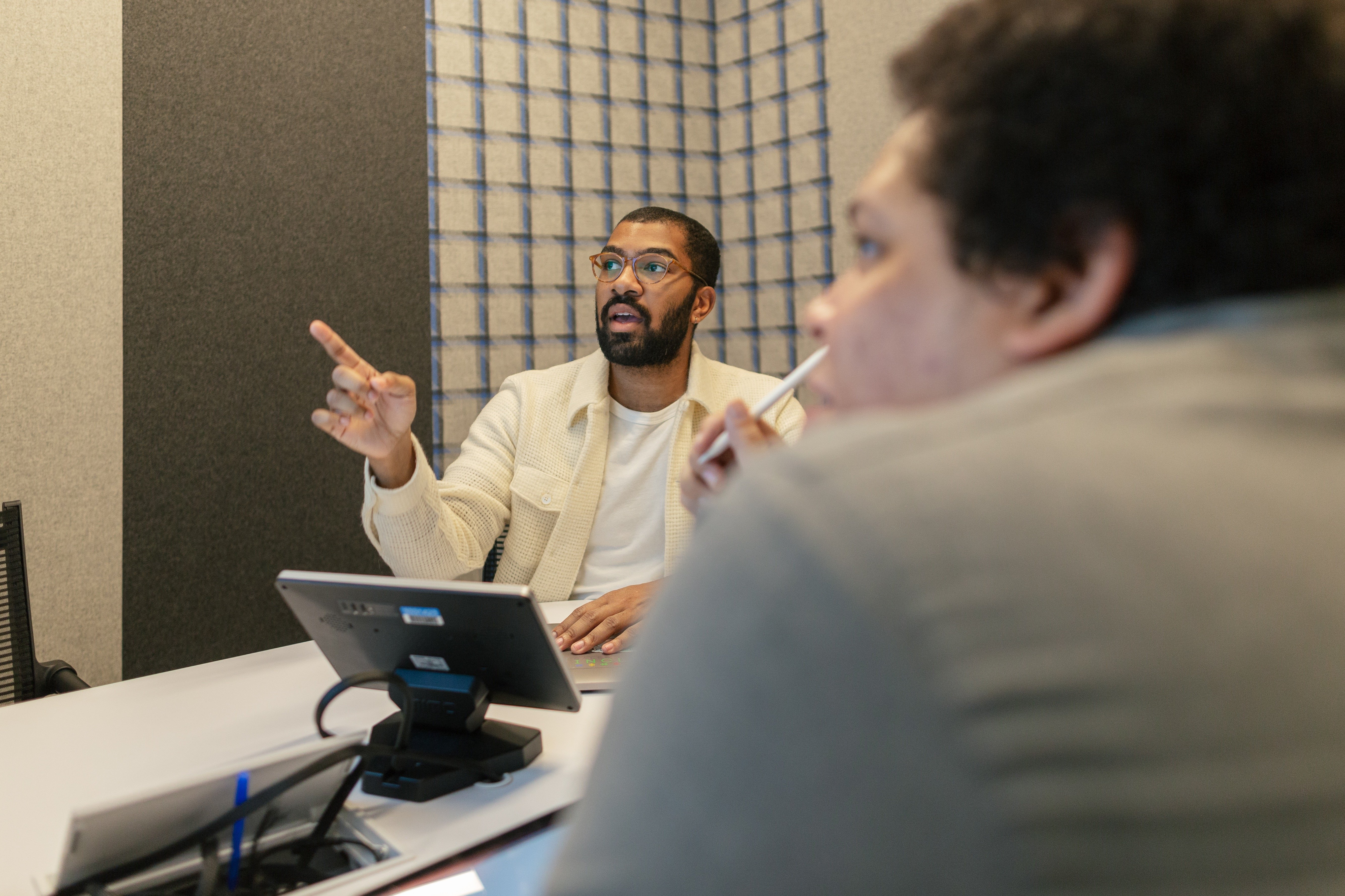 Two colleagues in a meeting room discuss something on a screen.