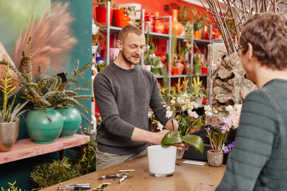 En blomsterhandler i sin butik, der omplanter en hvid orkidé i en hvid potte.