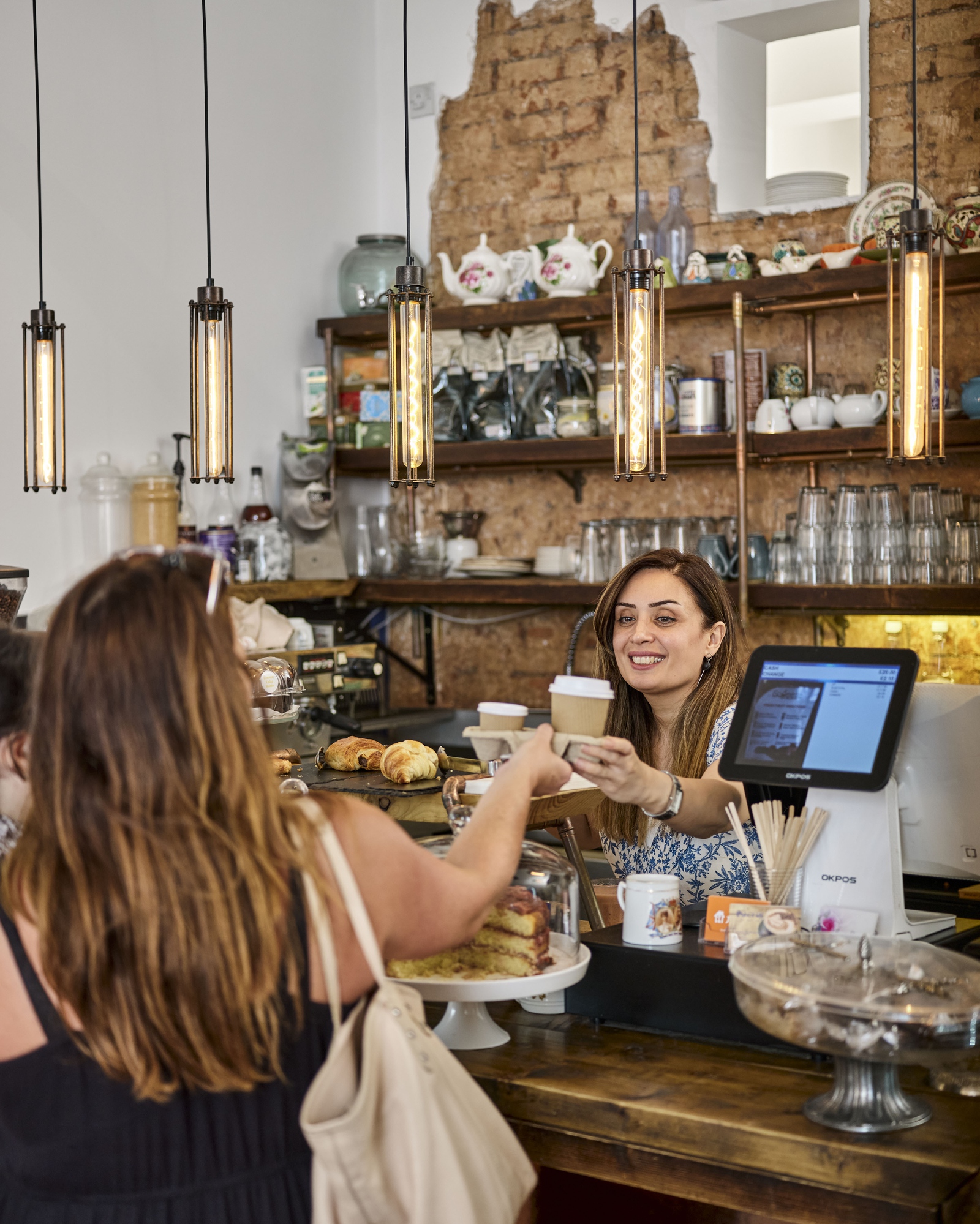 O femeie care lucreză într-o cafenea, oferă comanda zâmbind unei cliente.