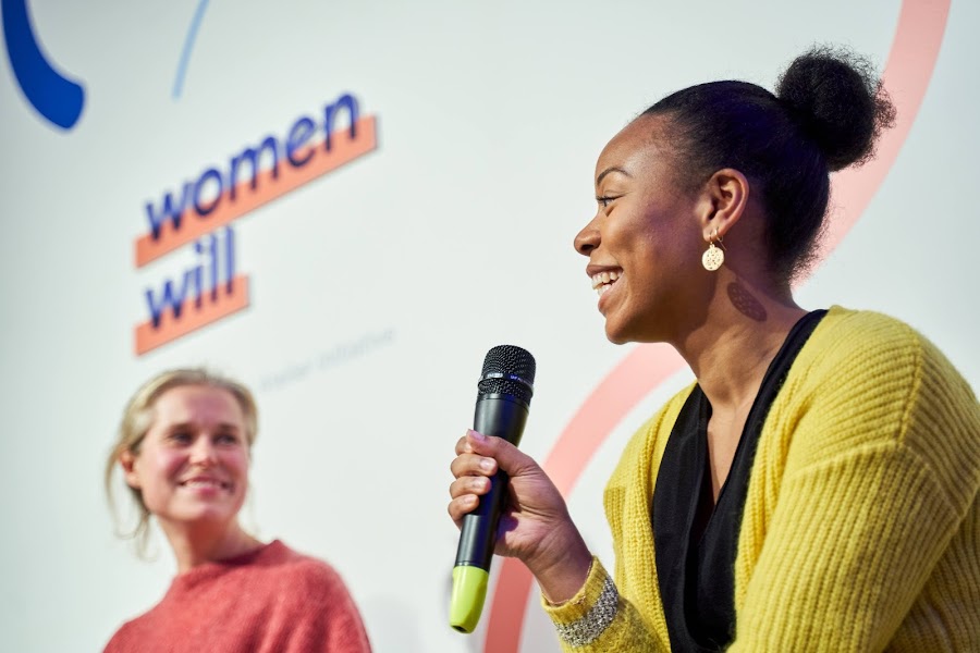 Ženska z nasmehom drži mikrofon na konferenci Women Will.