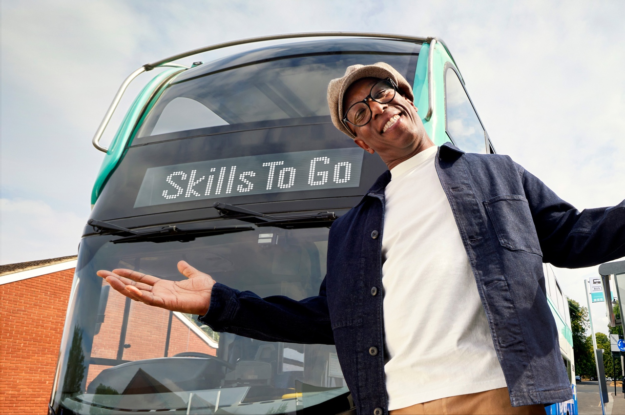 Ian Wright poses in front of a bus that reads "Skills to Go"