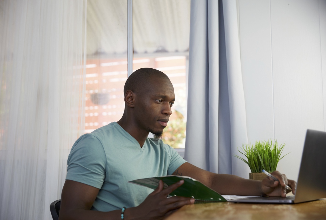 A bearded man in a roll neck jumper looks contented as he works on his laptop.