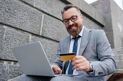 A man smiling in front of his laptop holding a credit card