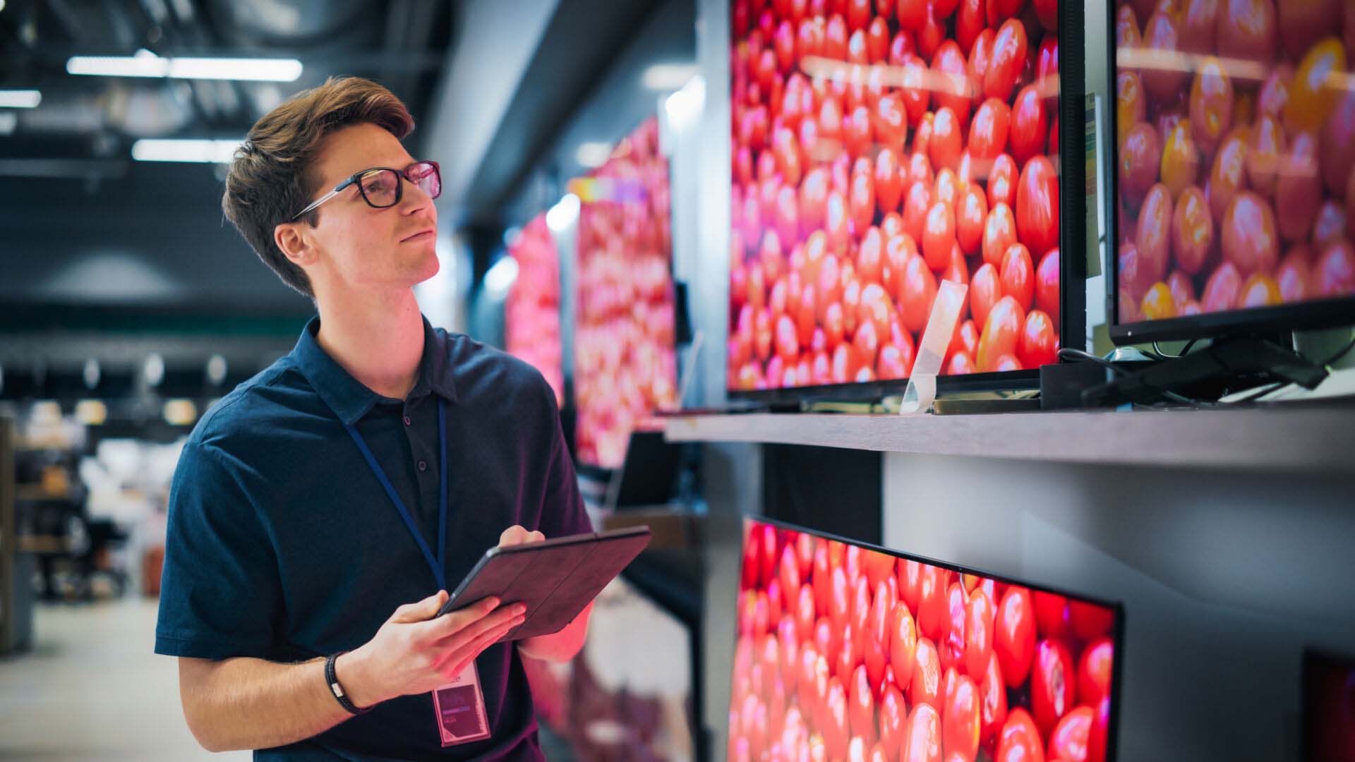 Young Sales Manager in Home Electronics Store Expertly Manages Operations Using Tablet. Professional Oversees TV Sets Inventory and Product Updates with Technological Efficiency. Insurance for Computer and Electronics Wholesalers