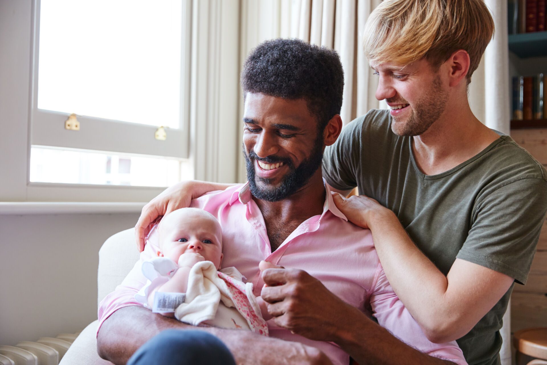Loving Male Same Sex Couple Cuddling Baby Daughter On Sofa At Home Together Insurance for Adoption Agencies