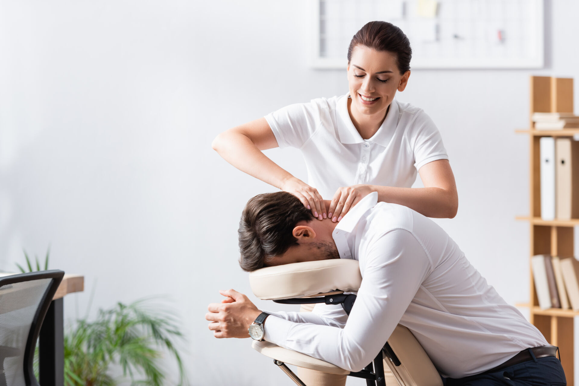 Happy masseuse doing neck massage for businessman in office on b Insurance for Massage Therapists