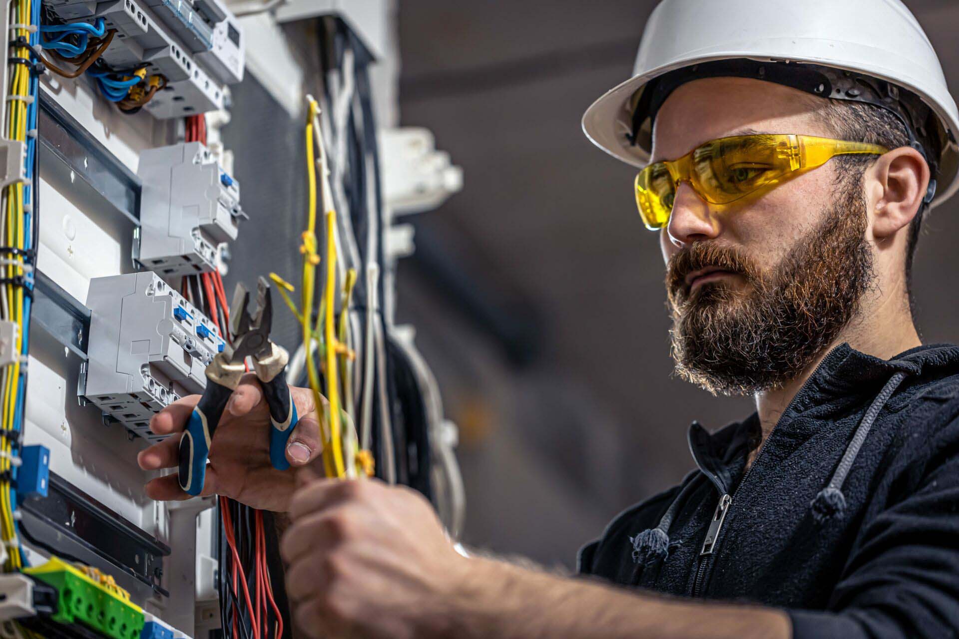 A male electrician works in a switchboard with an electrical connecting cable. Insurance for Electricians