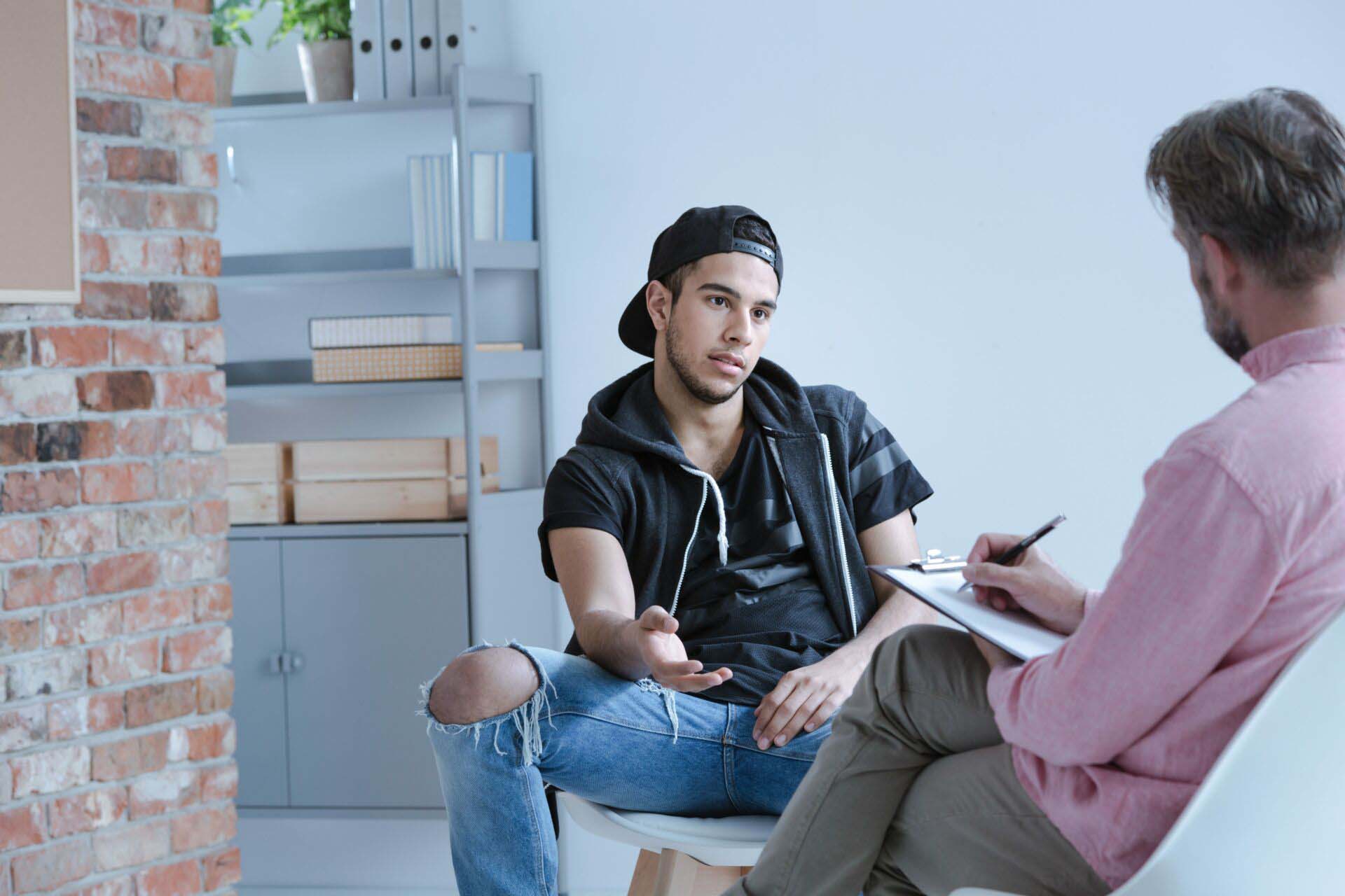 A rebel teenage boy with behavioral problems and criminal past talking to a psychotherapist in a juvenile detention center. Insurance for Counseling and Referral Centers