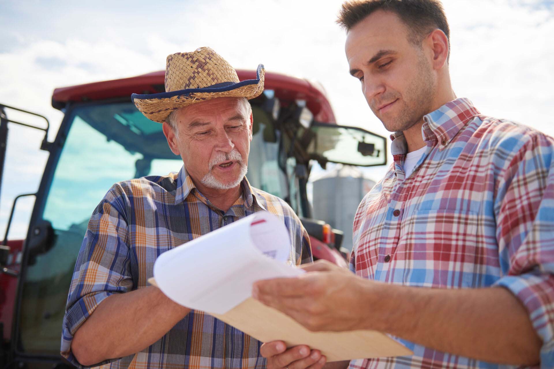 Two farmers discussing data from clipboard on the farm Insurance for Agricultural Consultants