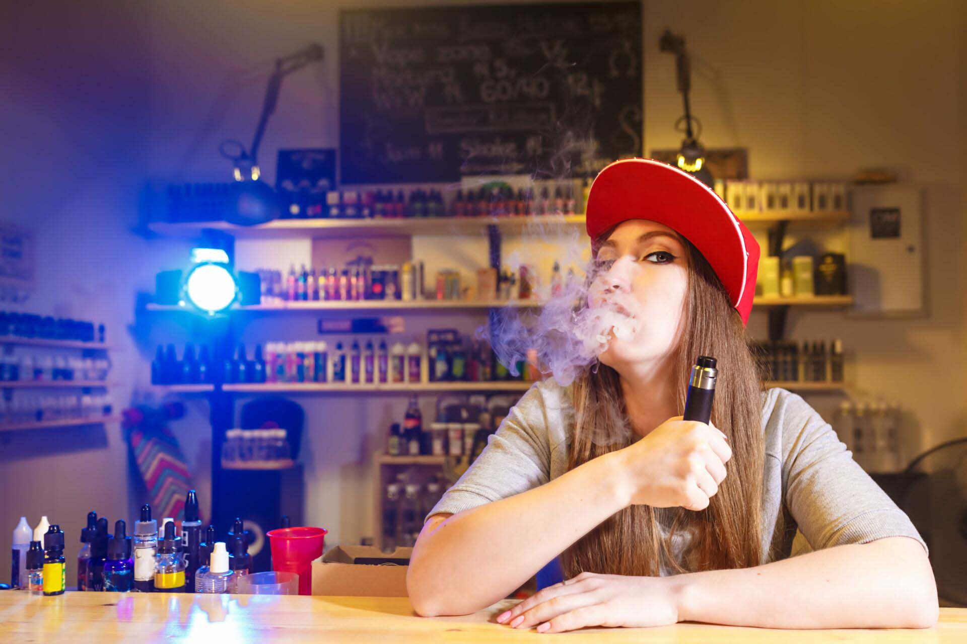 Young pretty woman in red cap smoke an electronic cigarette at the vape shop Insurance for Smoke, Tobacco, and Vape Shops