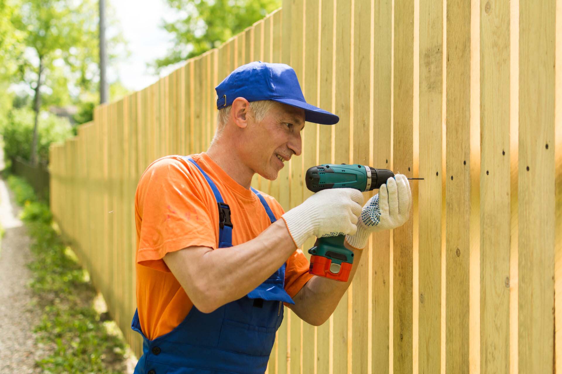 Handyman twirls a screw into the wooden fence wearily smiling Insurance for Fence Installation Contractors